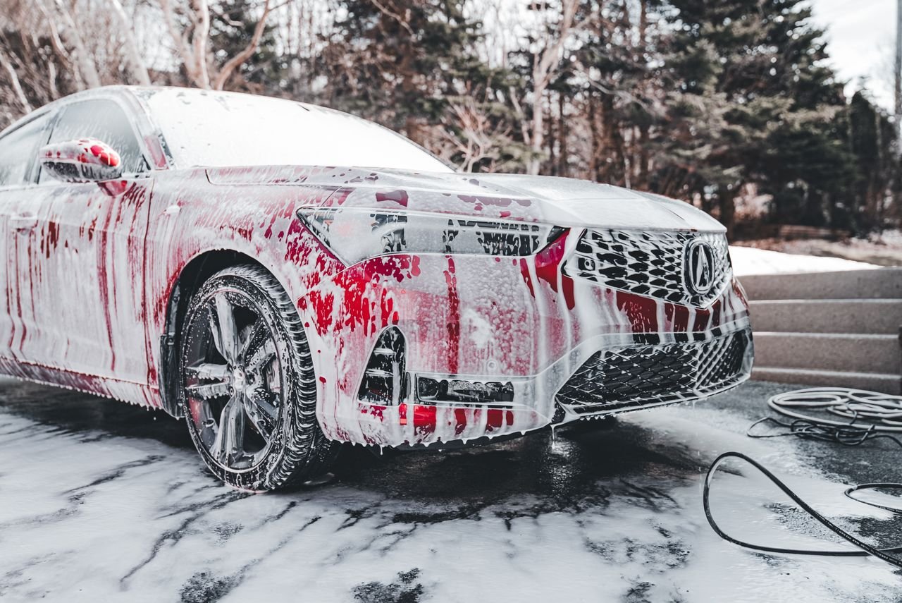 Crafting Captivating Headlines: Your awesome post title goes here A vibrant red car covered in soapy foam during a thorough outdoor wash under daylight.